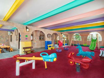 Zona de juegos interior colorida con toboganes, balancines y vigas de techo multicolor en área de hotel.