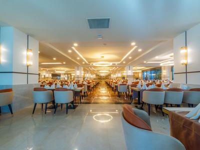 Amplio y luminoso comedor de hotel con muchas mesas y sillas modernas bajo luces cálidas en el techo.