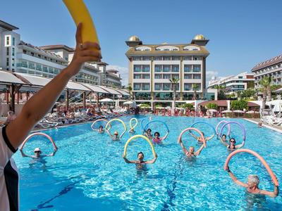 Menschen nehmen an Aquafitnesskurs im Hotelpool teil, angeleitet von Trainer mit gelbem Schwimmgerät.