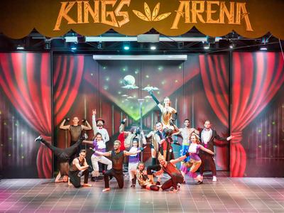 Menschen posieren vor einer Bühne mit Vorhängen und dem Schriftzug Kings Arena.