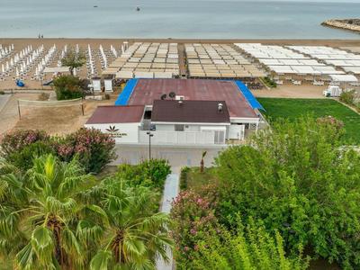 Vista aérea de un hotel con piscina, rodeado de palmeras y vista al mar con salinas.