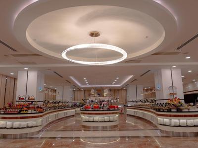 Amplia sala de buffet de hotel con mostradores curvos y luces modernas en el techo.