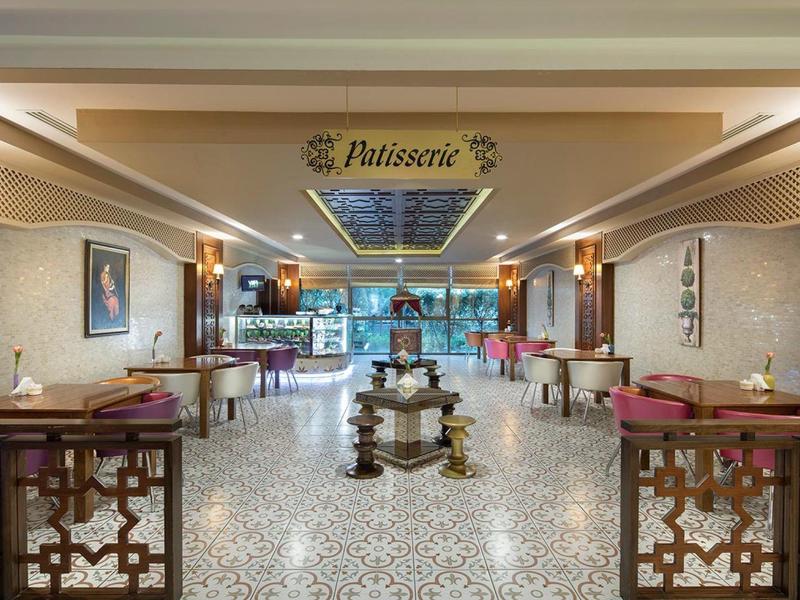 Cafetería elegante con suelo de azulejos decorativos y áreas de asiento acogedoras bajo un cartel de techo iluminado.