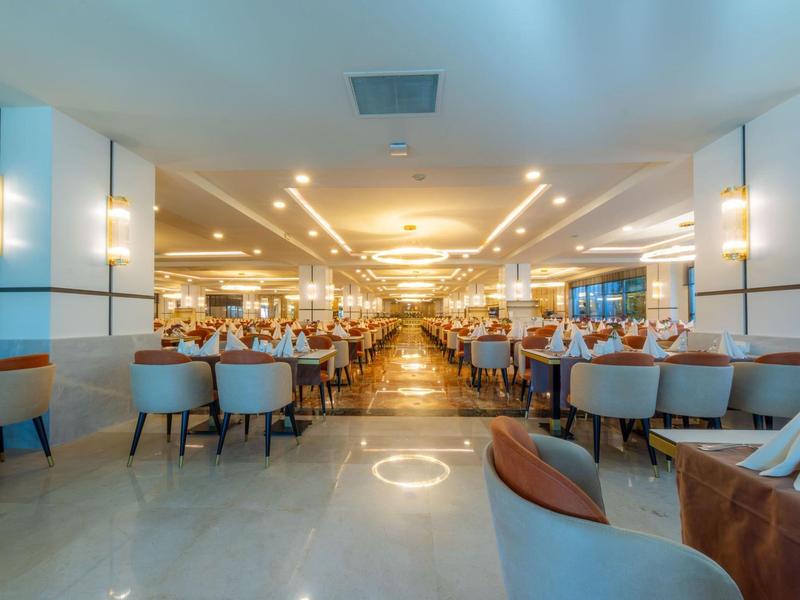 Amplio y luminoso comedor de hotel con muchas mesas y sillas modernas bajo luces cálidas en el techo.