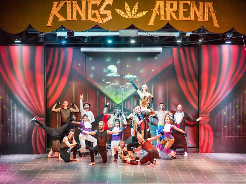 Un animado grupo de teatro posa frente a cortinas rojas bajo el letrero Kings Arena.