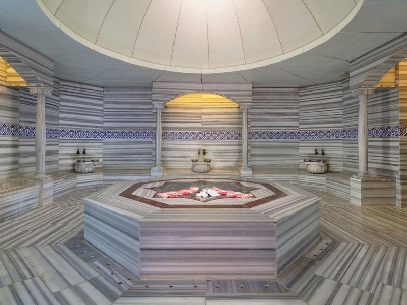 Gran hammam turco tradicional con suelo de mármol y estación de lavado central.
