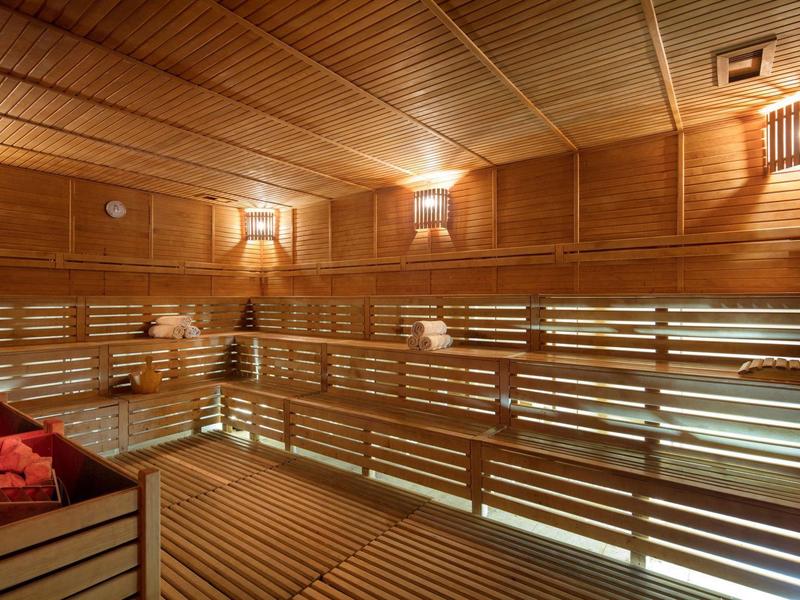 Vista interior de una sauna de madera con varios niveles de asientos y luz cálida.
