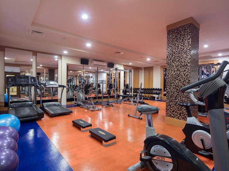 Gimnasio con cintas de correr, steppers, pesas y pelotas de ejercicio en habitación con luz cálida.