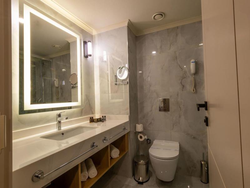 Baño moderno con espejo iluminado, lavabo y inodoro en tonos gris y beige.