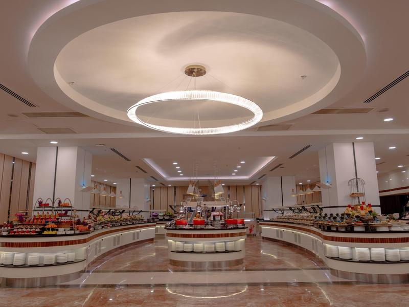 Amplia sala de buffet de hotel con mostradores curvos y luces modernas en el techo.