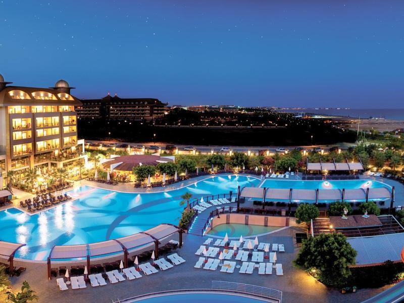 Resort hotelero de noche con piscina iluminada y tumbonas junto al mar