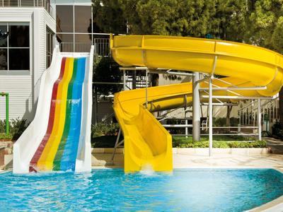Zwei Wasserrutschen, eine gelb und eine bunt, führen in einen Pool vor grüner Bepflanzung.