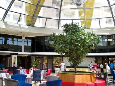 Luxuriöser Innenbereich mit Glasdach, großem Baum und modernem Sitzbereich in Blau und Rot.