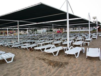 Muchas tumbonas blancas bajo grandes toldos en la playa de arena.