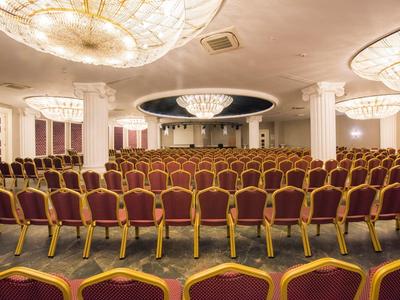 Gran sala de conferencias con muchas sillas rojas y grandes luces en el techo.