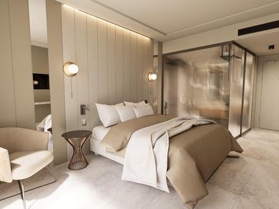 Habitación de hotel moderna con cama doble cómoda, zona de estar y ducha con mampara de vidrio.