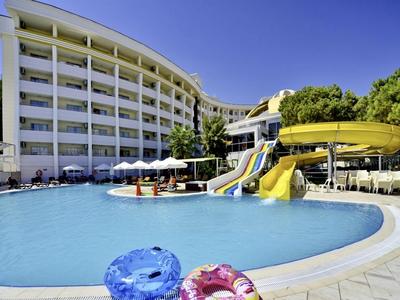 Großer Außenpool mit Wasserrutschen neben einem mehrstöckigen Hotel unter klarem Himmel.