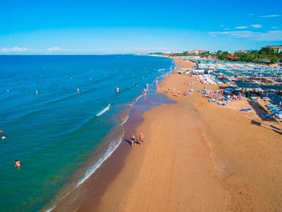 Weitläufiger Sandstrand mit zahlreichen Menschen und blauem Meer unter klarem Himmel.
