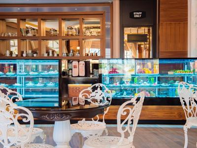 Elegantes Café mit weißen Metallstühlen und beleuchtetem Kuchenbuffet