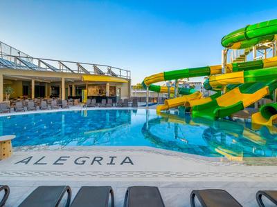 Grande piscina all'aperto con scivoli d'acqua verdi e lettini sotto il cielo azzurro in un hotel.