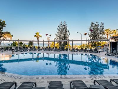 Piscina rotonda dell'hotel con lettini sotto un cielo sereno e palme sullo sfondo.