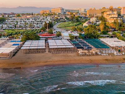 Ampia spiaggia con lettini davanti a più hotel sul mare al tramonto.