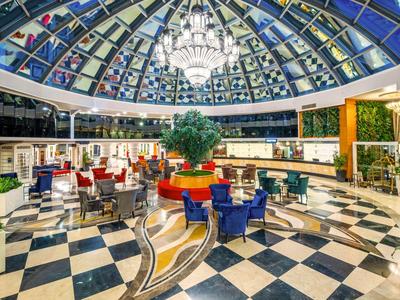 Ampio ed elegante atrio d'hotel con cupola in vetro, lampadario e sedute colorate.