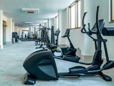 Sala fitness luminosa con varie attrezzature e grandi finestre.