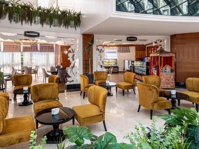 Lounge di hotel luminoso con poltrone gialle, piante e grandi finestre
