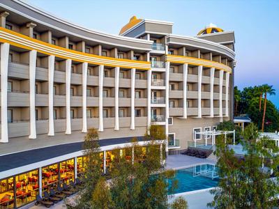 Hotel moderno con facciata curva e piscina, circondato da alberi al crepuscolo.