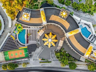 Vista aerea di un hotel moderno con piscine, campo da tennis e vegetazione circostante.