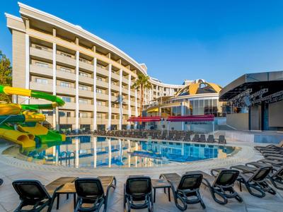 Hotel con piscina all'aperto, scivolo d'acqua e lettini sotto un cielo azzurro.