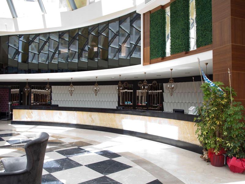 Moderno vestíbulo de hotel con mostrador de recepción curvo y plantas grandes.