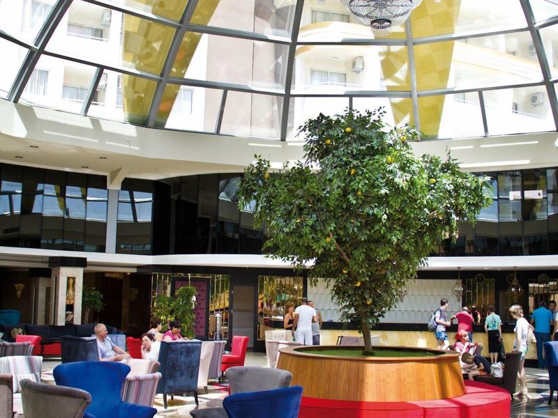 Interior lujoso con techo de cristal, gran árbol y área de asientos moderna azul y roja.