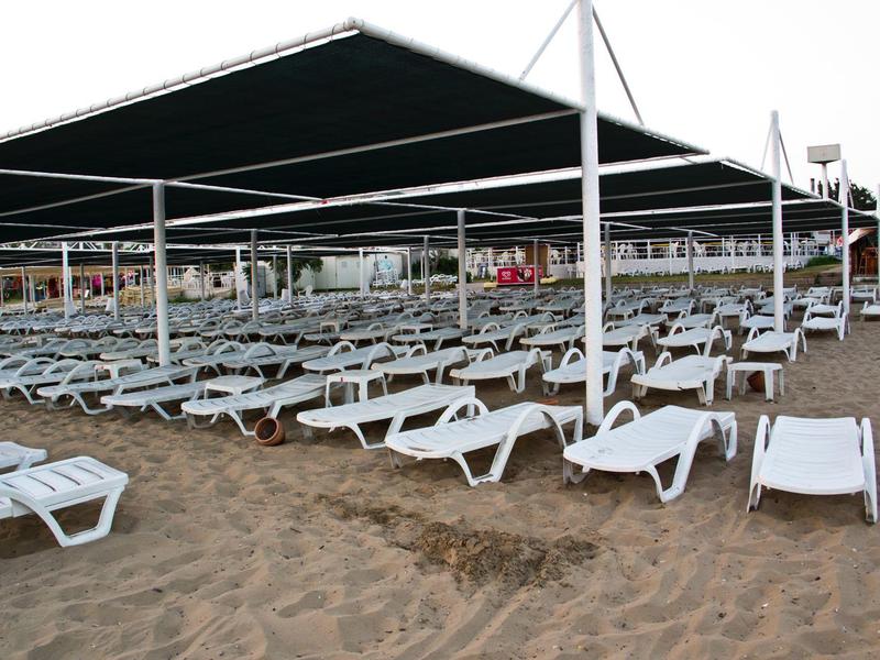 Muchas tumbonas blancas bajo grandes toldos en la playa de arena.