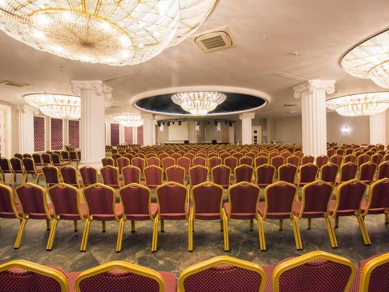 Gran sala de conferencias con muchas sillas rojas y grandes luces en el techo.