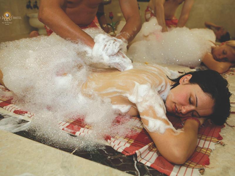 Dos hombres reciben masajes de espuma sobre esteras tradicionales en un área de spa.