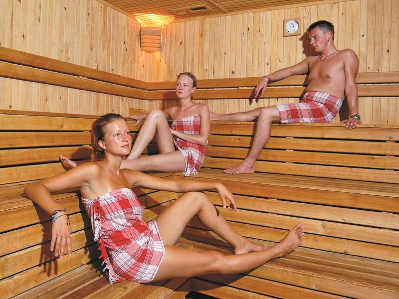Tres personas descansan en una sauna de madera sobre diferentes bancos.