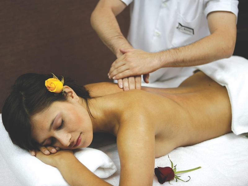 Mujer relajándose durante un masaje de espalda con una flor amarilla en el cabello.