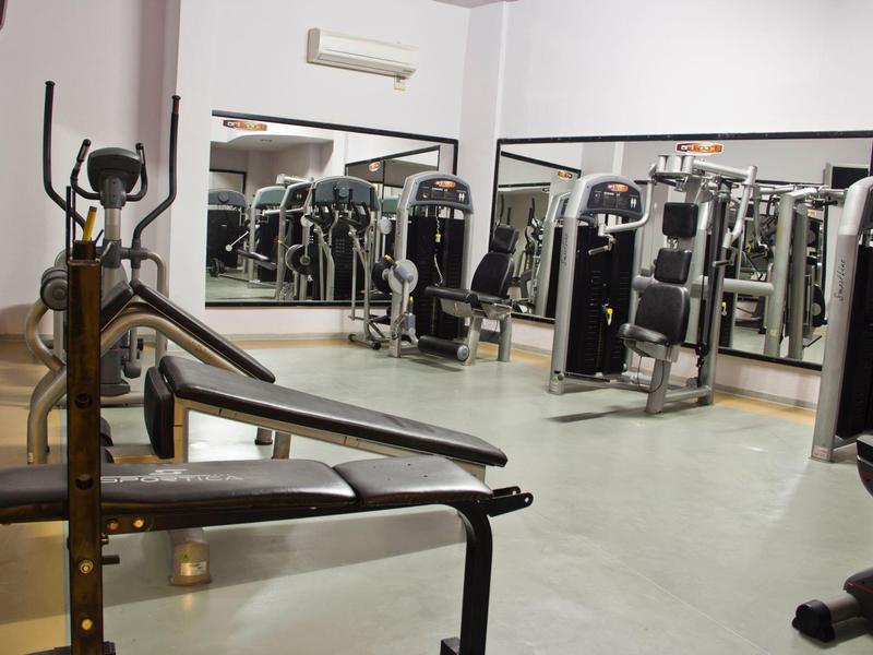 Interior de un gimnasio moderno con varias máquinas de ejercicio y grandes espejos en la pared.