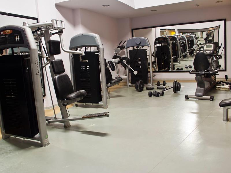 Gimnasio moderno con varias máquinas de ejercicio y un gran espejo en la pared.