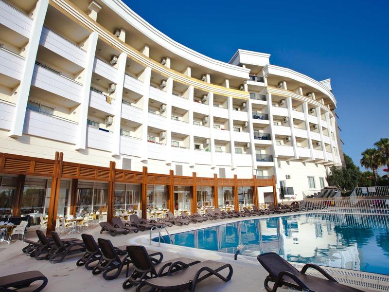 Edificio de hotel moderno con habitaciones con balcón y piscina bajo un cielo despejado.
