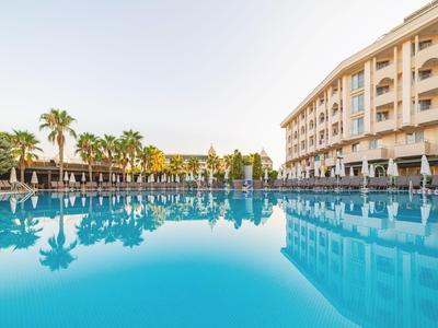 Groot hotelzwembad met ligstoelen en palmbomen op een zonnige dag