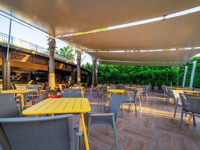 Taras na zewnątrz z stołami, krzesłami, żaglami przeciwsłonecznymi i palmami w hotelu.