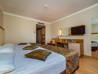 Jasny pokój hotelowy z dwoma łóżkami, telewizorem na ścianie i drewnianą podłogą.