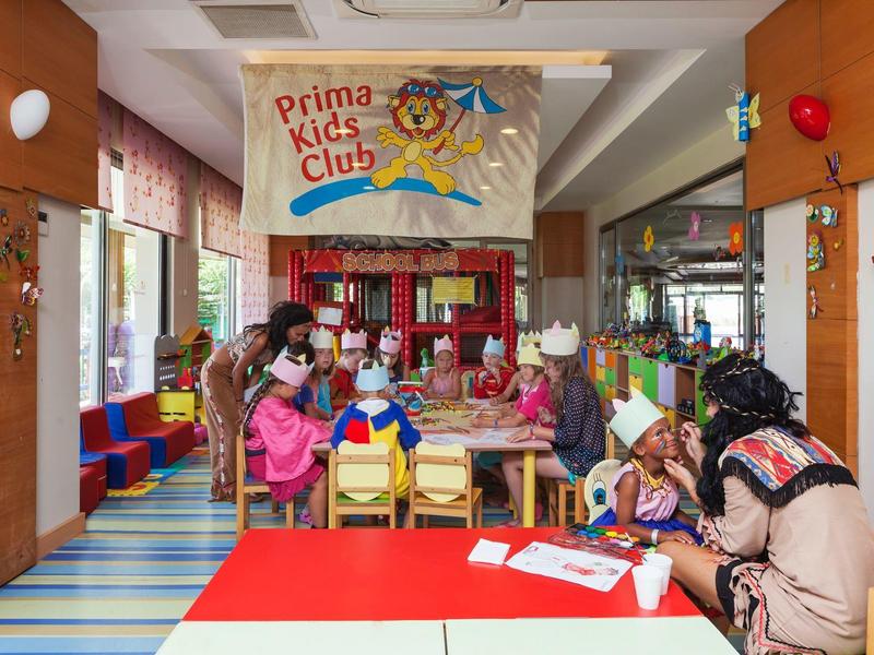 Kolorowy klub dziecięcy z dorosłymi i dziećmi siedzącymi przy stole do zabawy w środku.