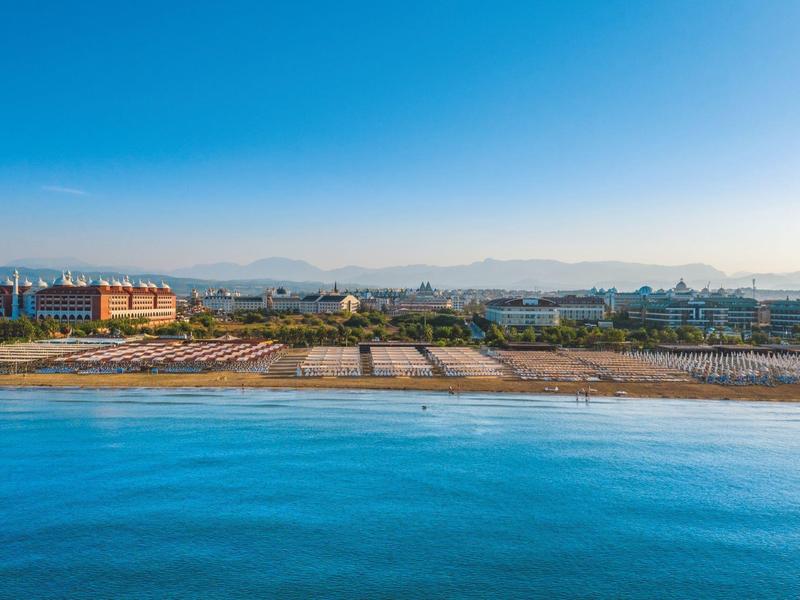 Plaża z leżakami przed kompleksem hotelowym i górami w tle pod czystym niebem