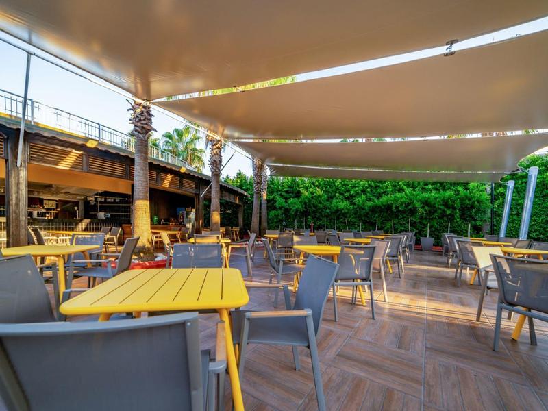 Taras na zewnątrz z stołami, krzesłami, żaglami przeciwsłonecznymi i palmami w hotelu.