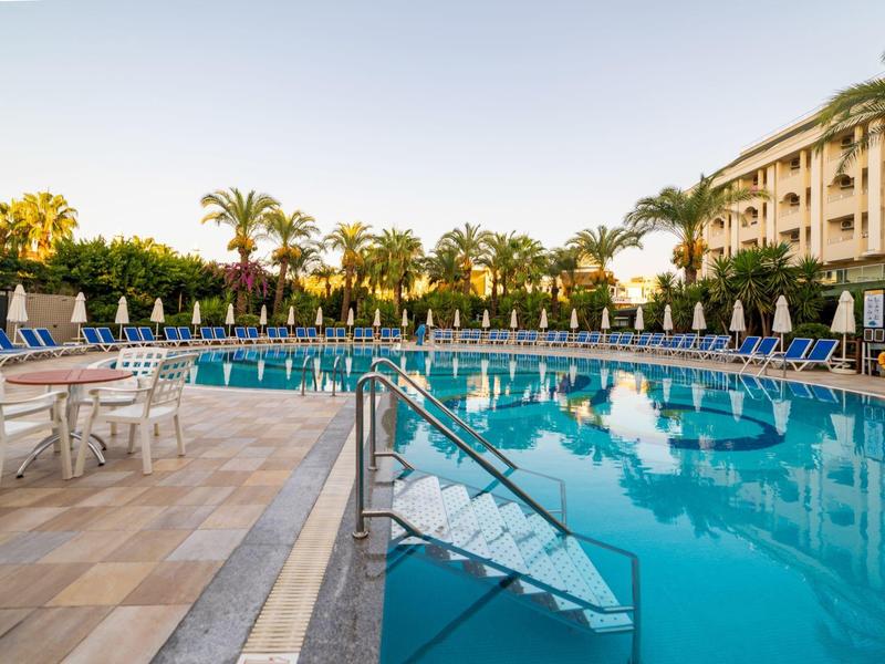 Duży basen hotelowy z palmami i leżakami w słoneczny dzień.