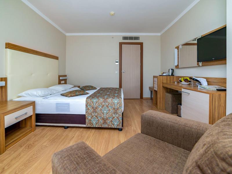 Nowoczesny pokój hotelowy z łóżkiem podwójnym, częścią wypoczynkową i drewnianą podłogą.